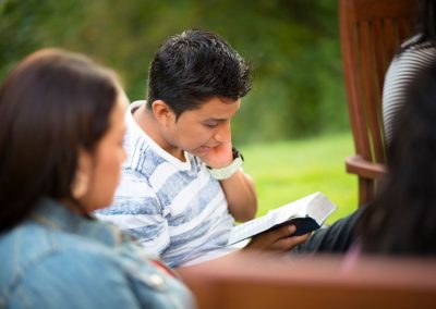 boy reading his scriptures next to a woman who is out of focus